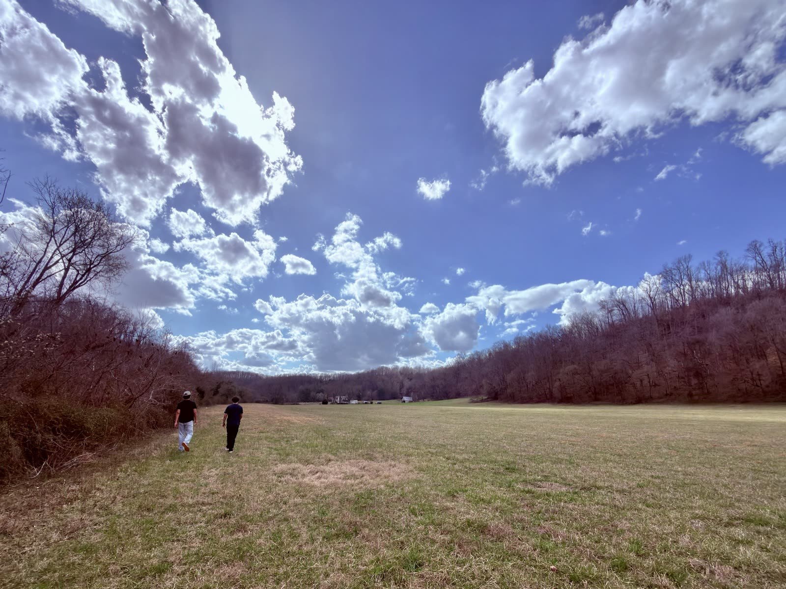 Two crew members walk across the open Tennessee field beneath a wide, clouded sky.