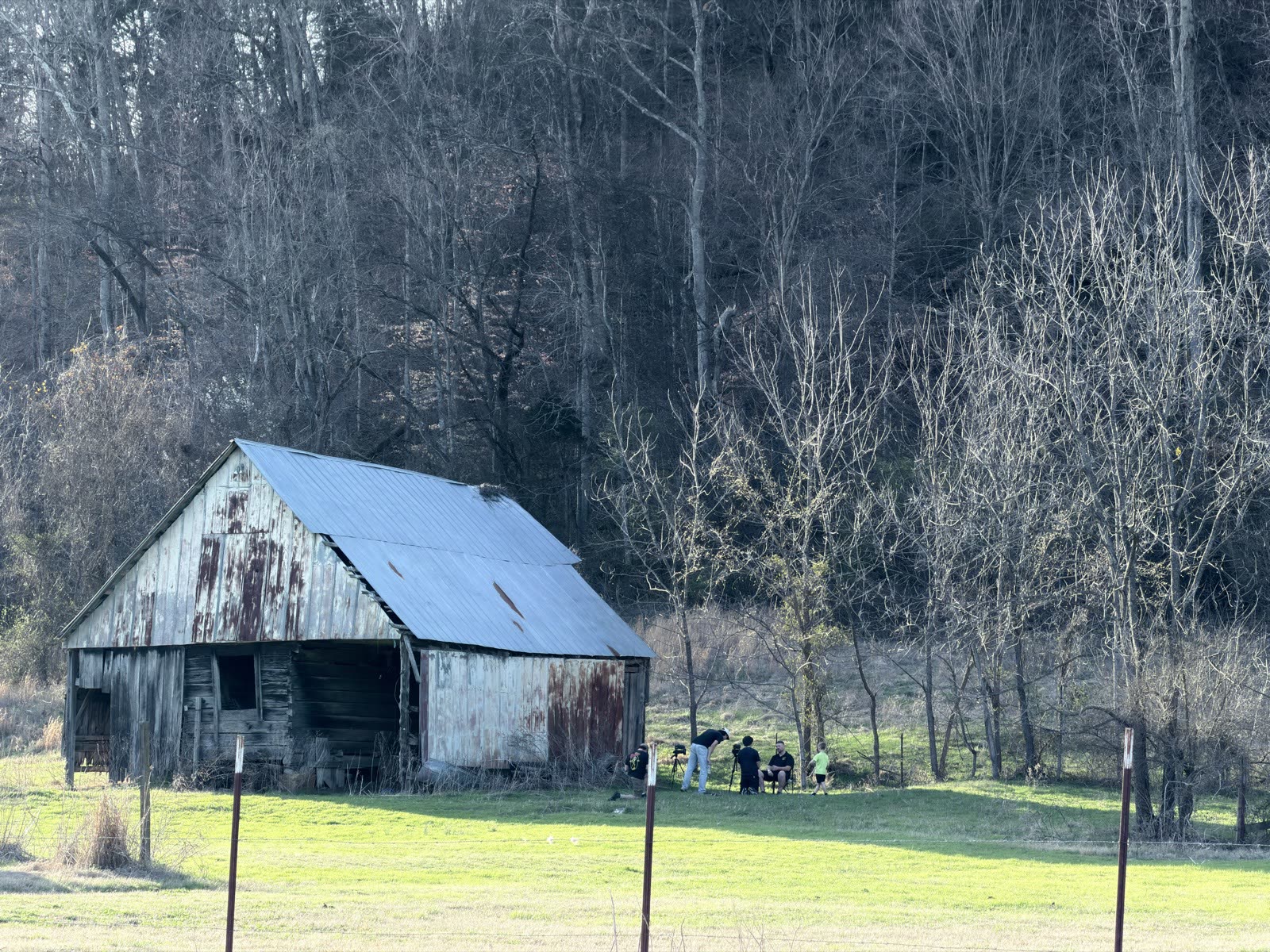 Seen from across the field, the crew films an interview beside the old barn.