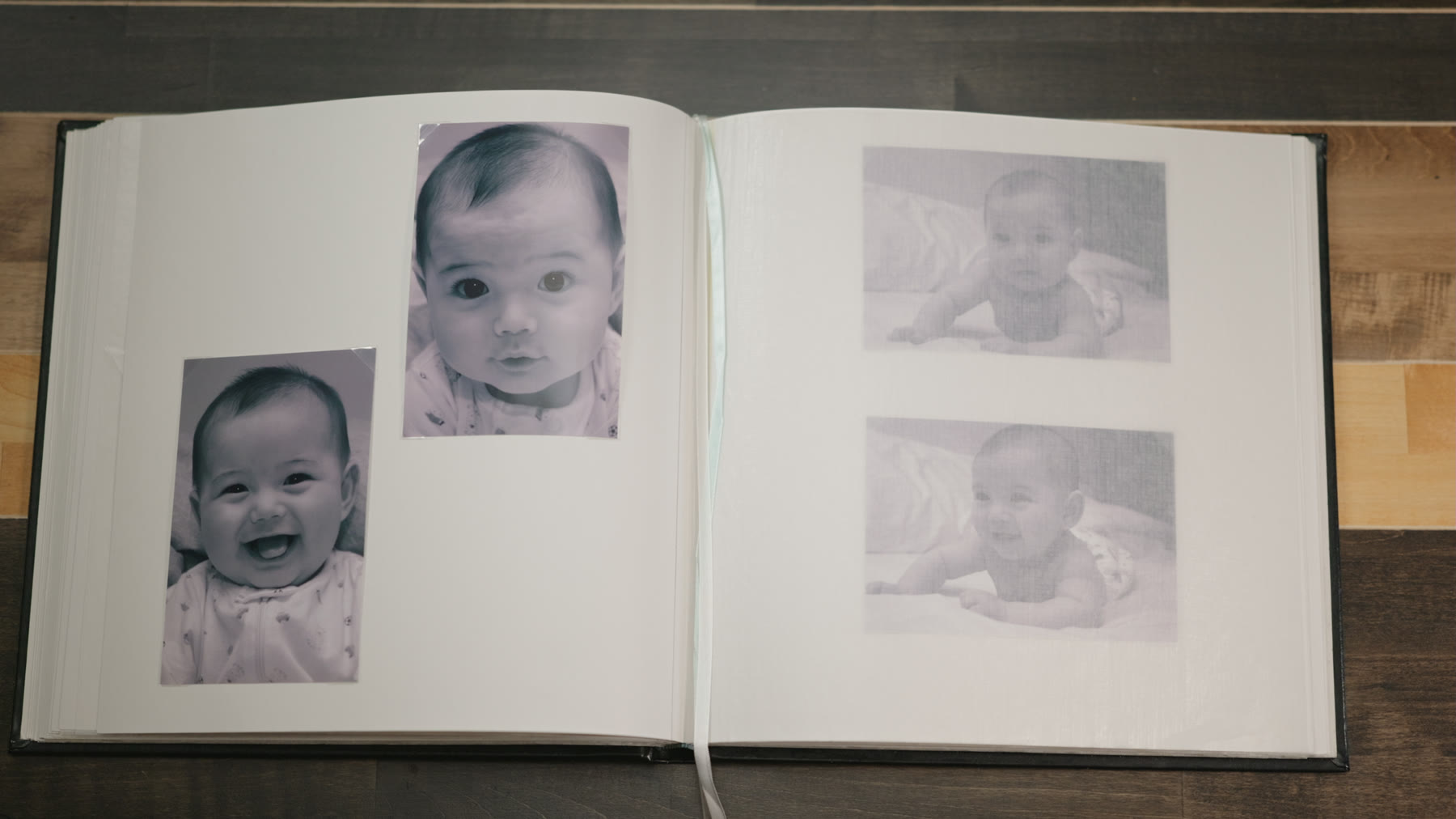 An open family photo album on a wooden table, filled with baby photographs.